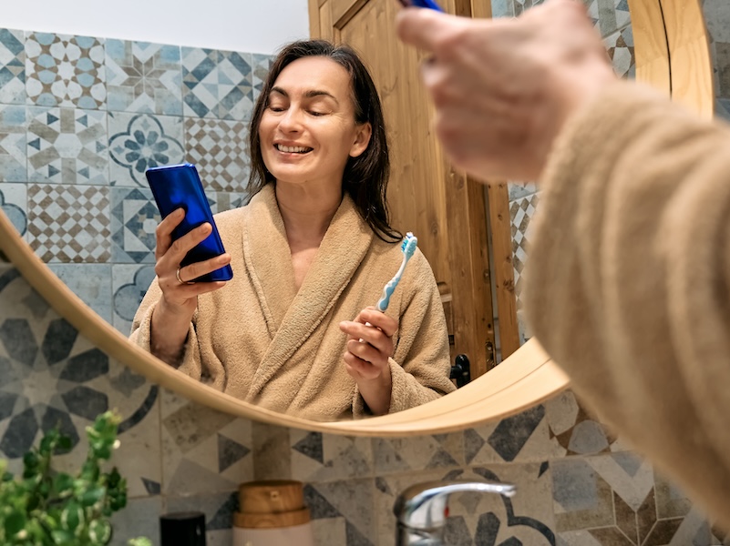Woman brushing teeth and using smartphone.