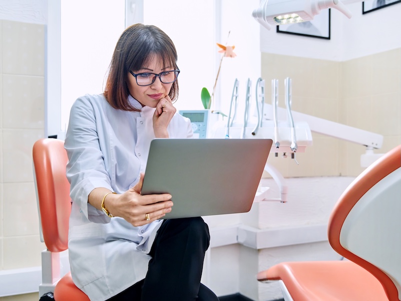 Female dentist in treatment room looking at laptop