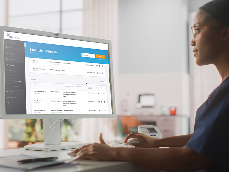 Woman in office works on a desktop computer with the TrueLark customer communications platform dashboard on the monitor.